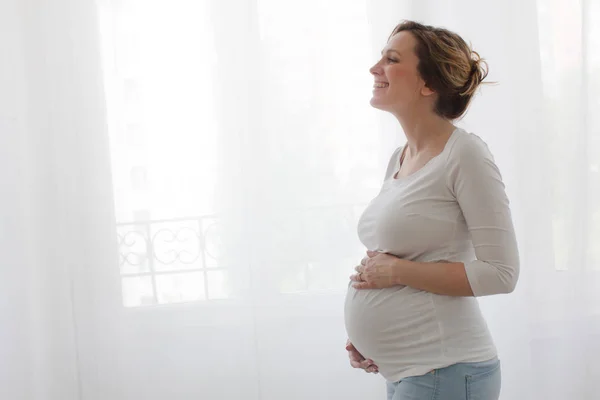 Szczęśliwa Kobieta w ciąży dotykając brzuch i śmiejąc się — Zdjęcie stockowe
