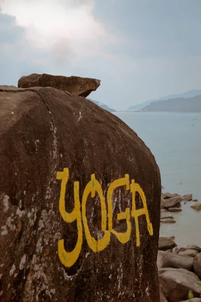 Duży kamień, w pobliżu oceanu z żółtym tytuł Yoga — Zdjęcie stockowe