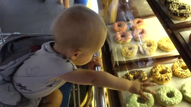 Boy boy reaches a showcase with donuts in coffee — Stock Video