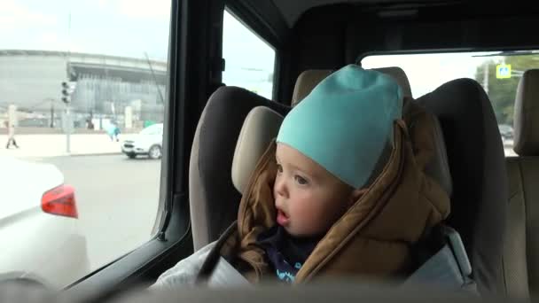 Малыш сидит в машине на стуле возле городских улиц — стоковое видео