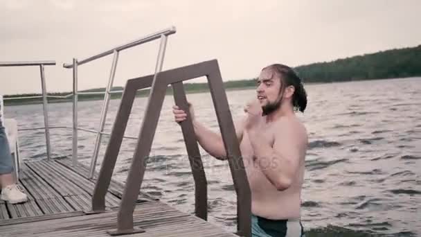 Молодой человек выходит из воды и позирует — стоковое видео