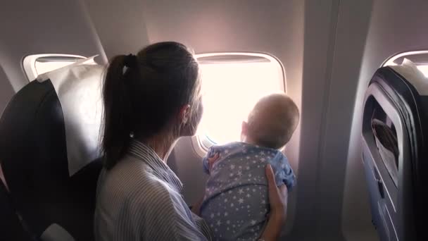 Mamãe e seu bebê no avião olham pela janela — Vídeo de Stock