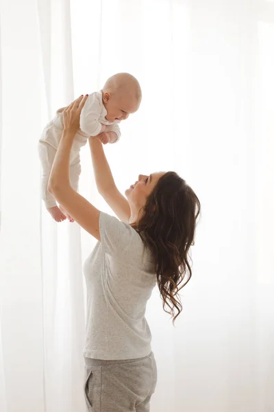 Anne bebek kollarında penceresi arka planını tutar — Stok fotoğraf