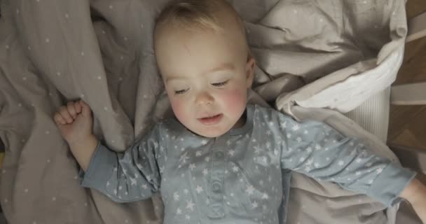 Bébé garçon est couché dans un lit et bavarde — Video