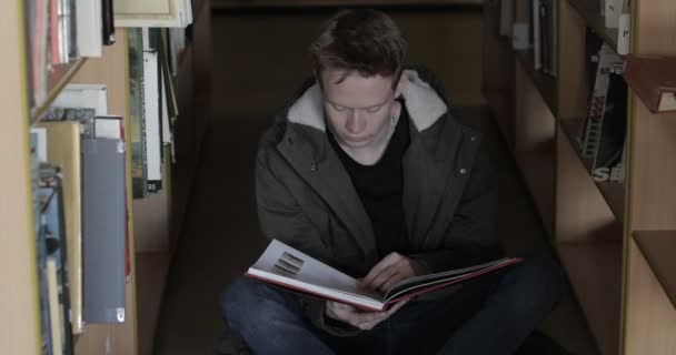 Estudiante sentado en el piso de la biblioteca leyendo libro — Vídeos de Stock