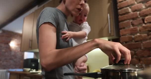 Madre está cocinando plato es mimado bebé en brazos — Vídeos de Stock