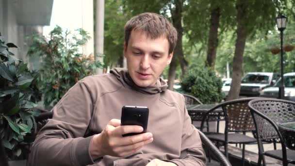 人读智能手机坐在咖啡馆在街上 — 图库视频影像