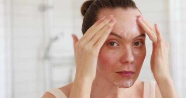 Woman applying moisturiser to her face in mirror — Stock Video