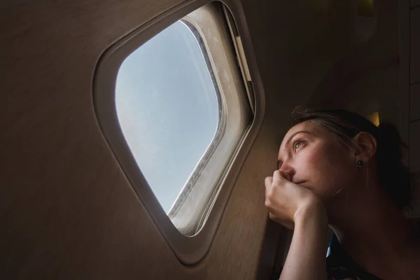 Грустная женщина в иллюминаторе в самолете — стоковое фото