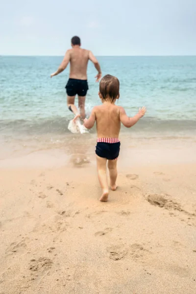 Pequeno bebê correndo com o homem na praia — Fotografia de Stock