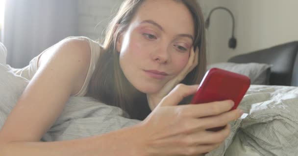 Šťastná žena leží na posteli s úsměvem text smartphone — Stock video