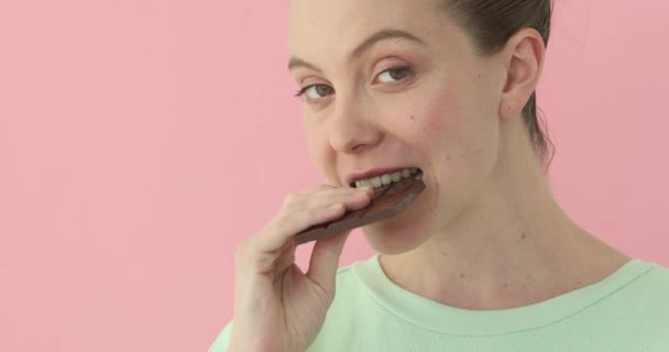ピンクの背景の上にチョコレートを食べる女性 — ストック動画