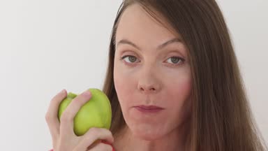 Genç kadın beyaz arka plan büyük bir yeşil elma yiyor. Meyve yeme sağlıklı beslenme modeli. Kız ilk ısırık alır ve sonra teklif görüntüleyici ve söyleyerek ister ısırmaya