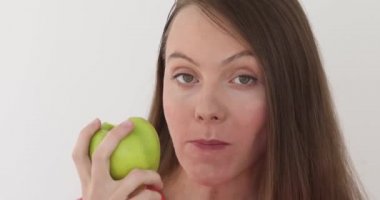 Genç kadın beyaz arka plan büyük bir yeşil elma yiyor. Meyve yeme sağlıklı beslenme modeli. Kız ilk ısırık alır ve sonra teklif görüntüleyici ve söyleyerek ister ısırmaya