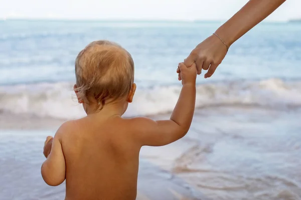 Mały dzieciak trzyma się za ręce z bezimienną mamą na plaży — Zdjęcie stockowe