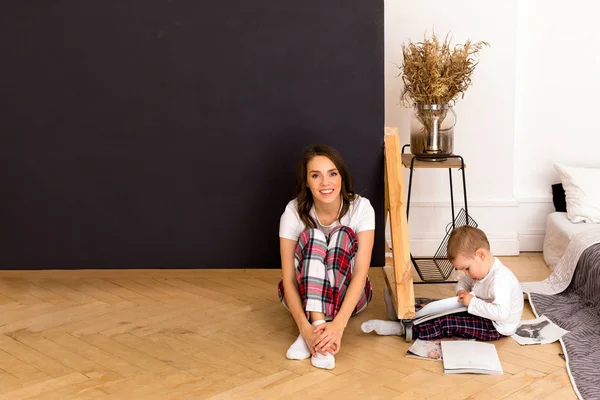 Son drawing on paper sitting on floor with happy mother
