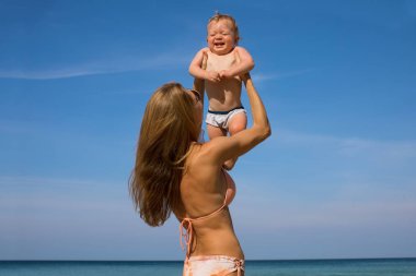 Mother holding happy little baby on beach