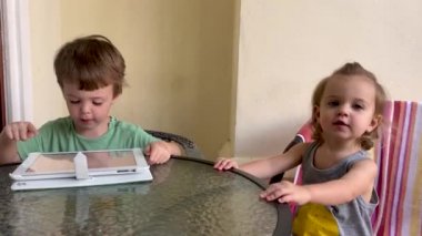Adorable kids sitting at table and having fun with tablet