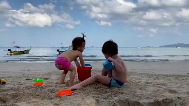 Niños alegres jugando con juguetes y arena en la playa en un día nublado — Vídeos de Stock
