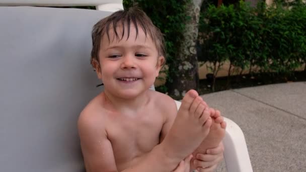 Joyeux petit garçon humide assis sur une chaise dans la cour — Video