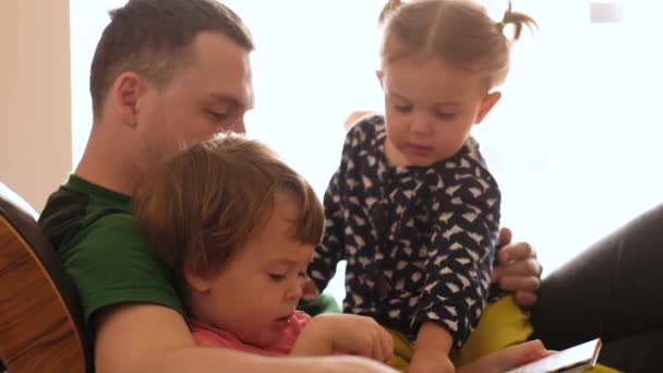 Отец читает книжку детям на диване — стоковое видео