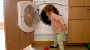 Funny little girl placing toys in washing machine