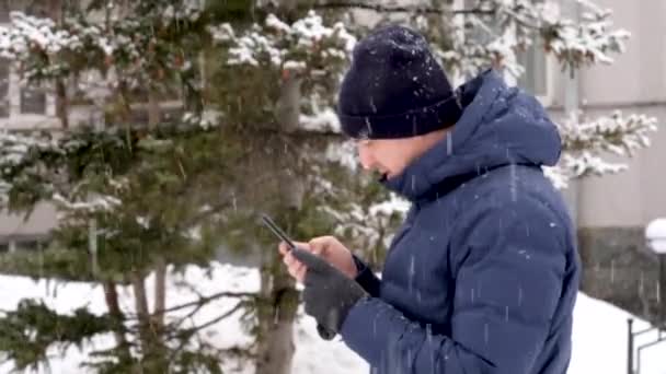 Человек, использующий смартфон в снежный день в городе — стоковое видео