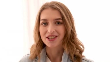 Genç bir kadın mavi arka planda kamerayla konuşuyor.