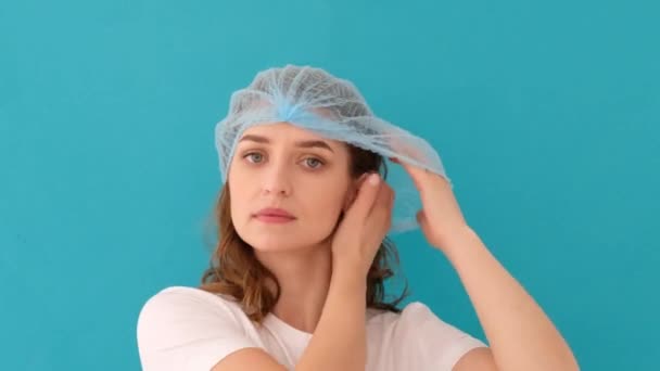Calm young woman putting on blue medical hat — Stock Video