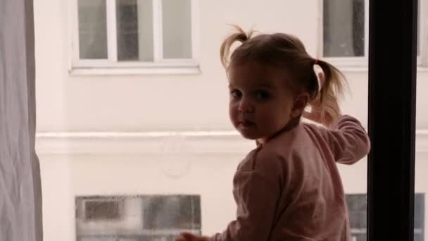 Ciekawa dziewczynka wyglądająca przez okno. — Wideo stockowe