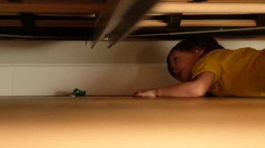 Çocuk yatağın altındaki oyuncağa uzanır