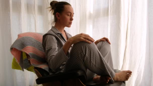 Femme en pyjama méditant sur chaise — Video