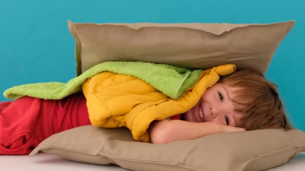 Мальчик прячется в подушки на голубом фоне — стоковое видео