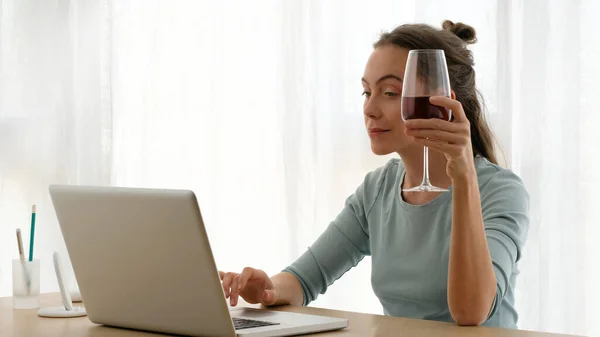 Mujer trabajando en un portátil con una copa de vino — Foto de Stock