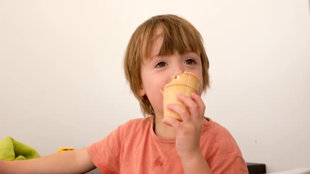 Маленький хлопчик із задоволенням їсть морозиво, відпочиваючи вдома — стокове відео