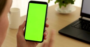 Kadının elinde yeşil ekranlı bir telefon var.