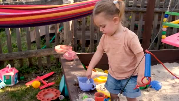 Serio niño pequeño jugando juguetes en sandbox en el patio trasero en verano día soleado — Vídeos de Stock