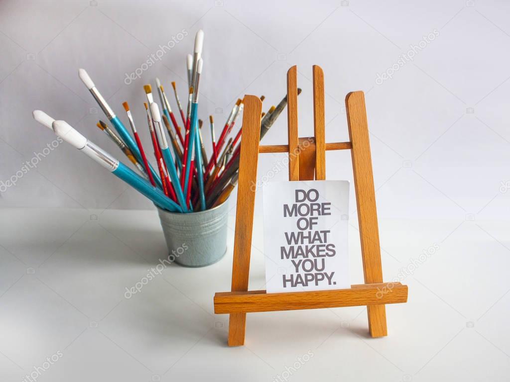Still life with brushes, easel with small poster (Do more of what makes you happy)