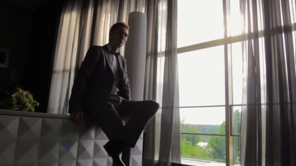 Молодой человек, сидящий у окна — стоковое видео