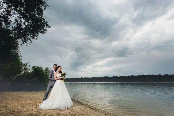 Recém-casados abraçando na margem do rio — Fotografia de Stock