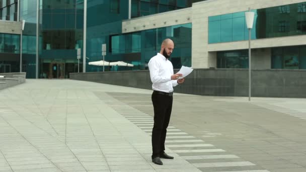 Бизнесмен швыряет бумагу возле офисного здания — стоковое видео