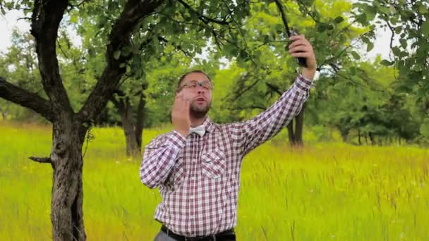 Homem de óculos ficando no prado e fazendo selfie — Vídeo de Stock