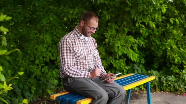 Человек с сенсорным блокнотом сидит в парке, что-то ищет — стоковое видео