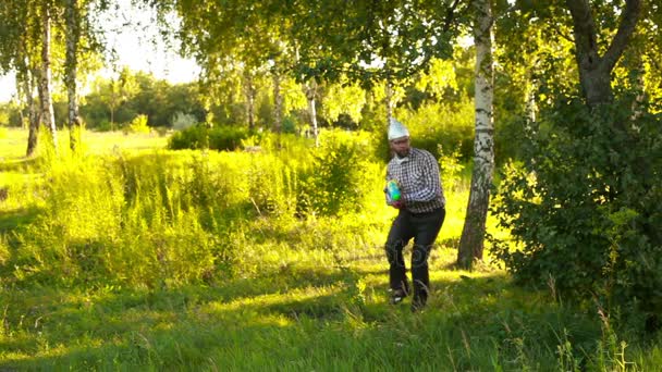 Junger Mann mit Kapuze schleicht langsam mit Spielzeugpistole durch den Wald — Stockvideo