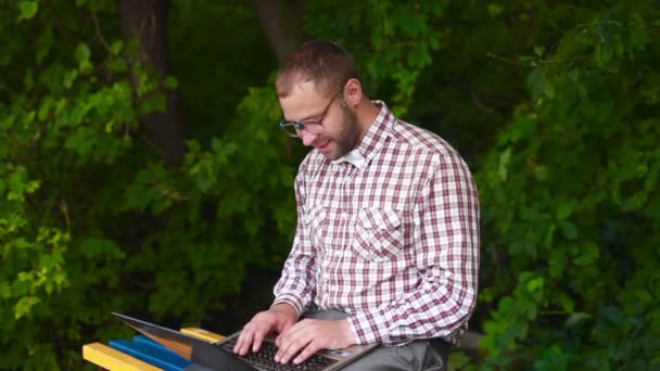 Mladý muž v brýlích, sedí na lavičce v parku — Stock video