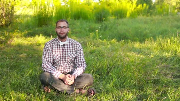 Çimenlerin üzerinde oturan gözlüklü genç adam — Stok video