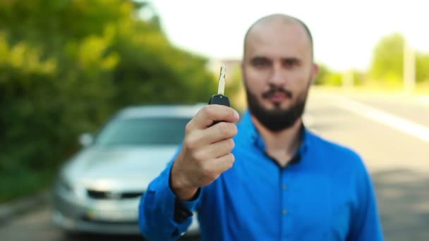 Smiling man with beard in front of car showing key — Stock Video