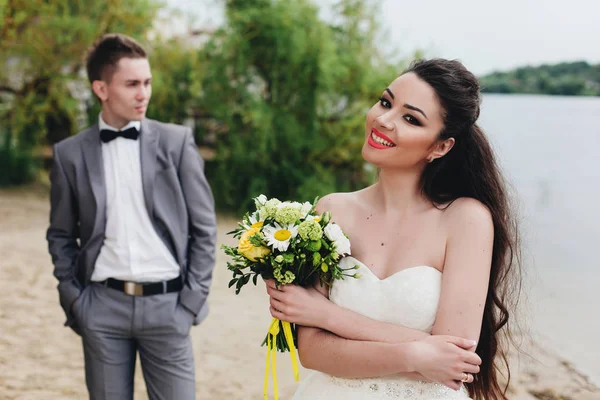 Novia con novio detrás en la orilla del río — Foto de Stock