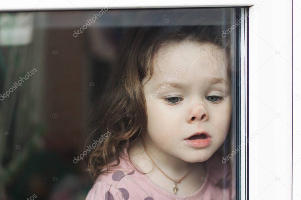 The girl at home behind the glass, looking out the window, leaning her nose