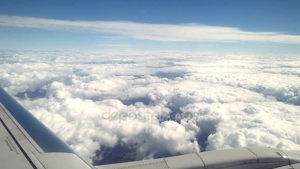 Tierra y nubes blancas bajo el ala de un avión durante el vuelo — Vídeos de Stock